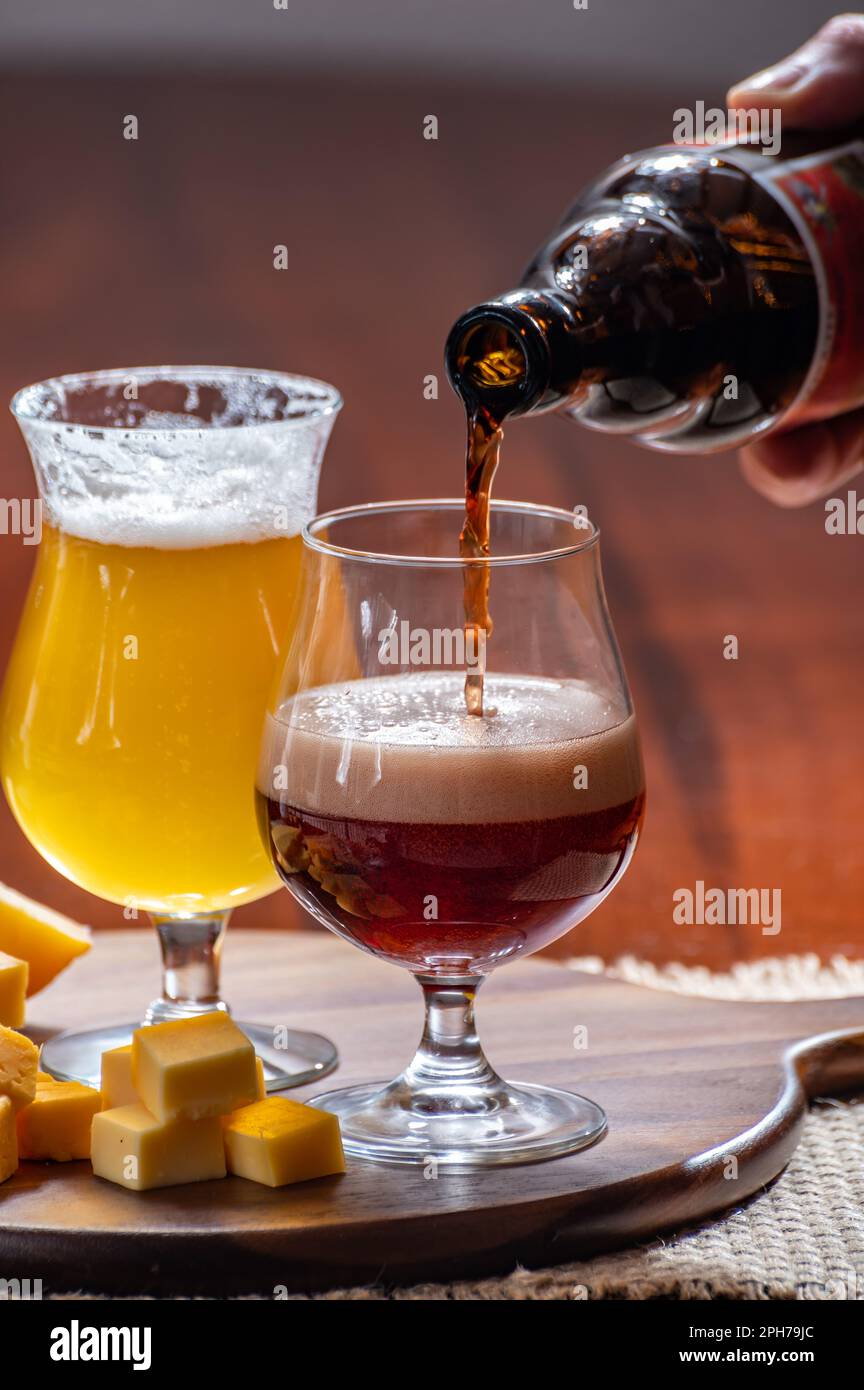 Verres de bière blonde jaune belge et brune foncée fabriqués en abbaye et en bois avec une variété de fromages belges, plats et bières assortis en Belgique Banque D'Images