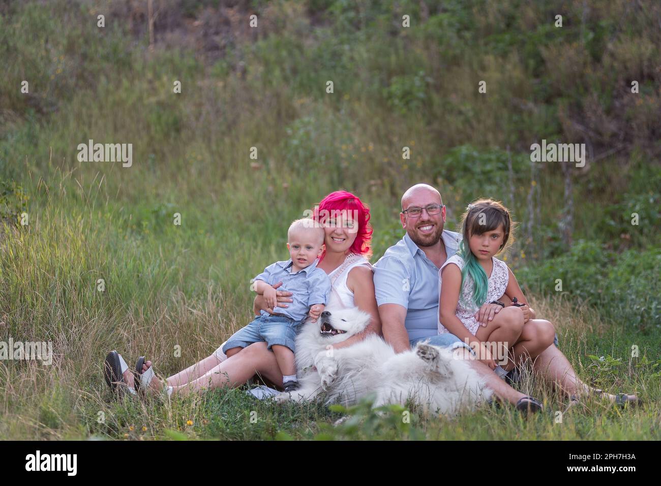 Portrait de famille lumineuse, inhabituelle, diversité dans la nature avec le chien Samoyed. Voyager avec des animaux de compagnie. Les créatifs regardent la caméra. Bac botanique vert Banque D'Images