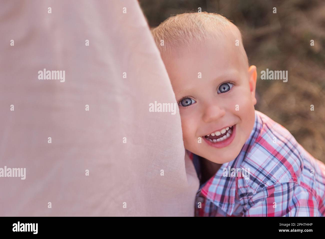 Gros plan du petit garçon en chemise à carreaux, qui épouse la jambe de la mère. Vue de dessus d'un tout-petit souriant avec des yeux bleus. Le concept de protection parentale, t Banque D'Images