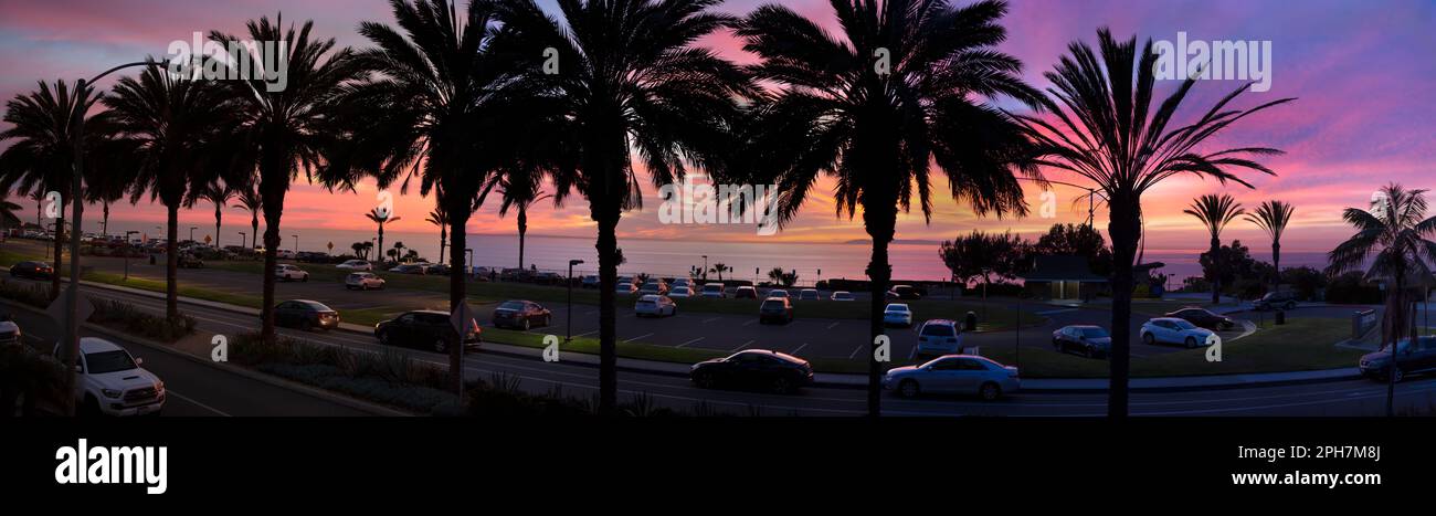 Coucher de soleil sur la côte ouest au-dessus d'un parking de voitures, de palmiers et de l'océan Pacifique à Dana point, comté d'Orange, Californie du Sud. Banque D'Images