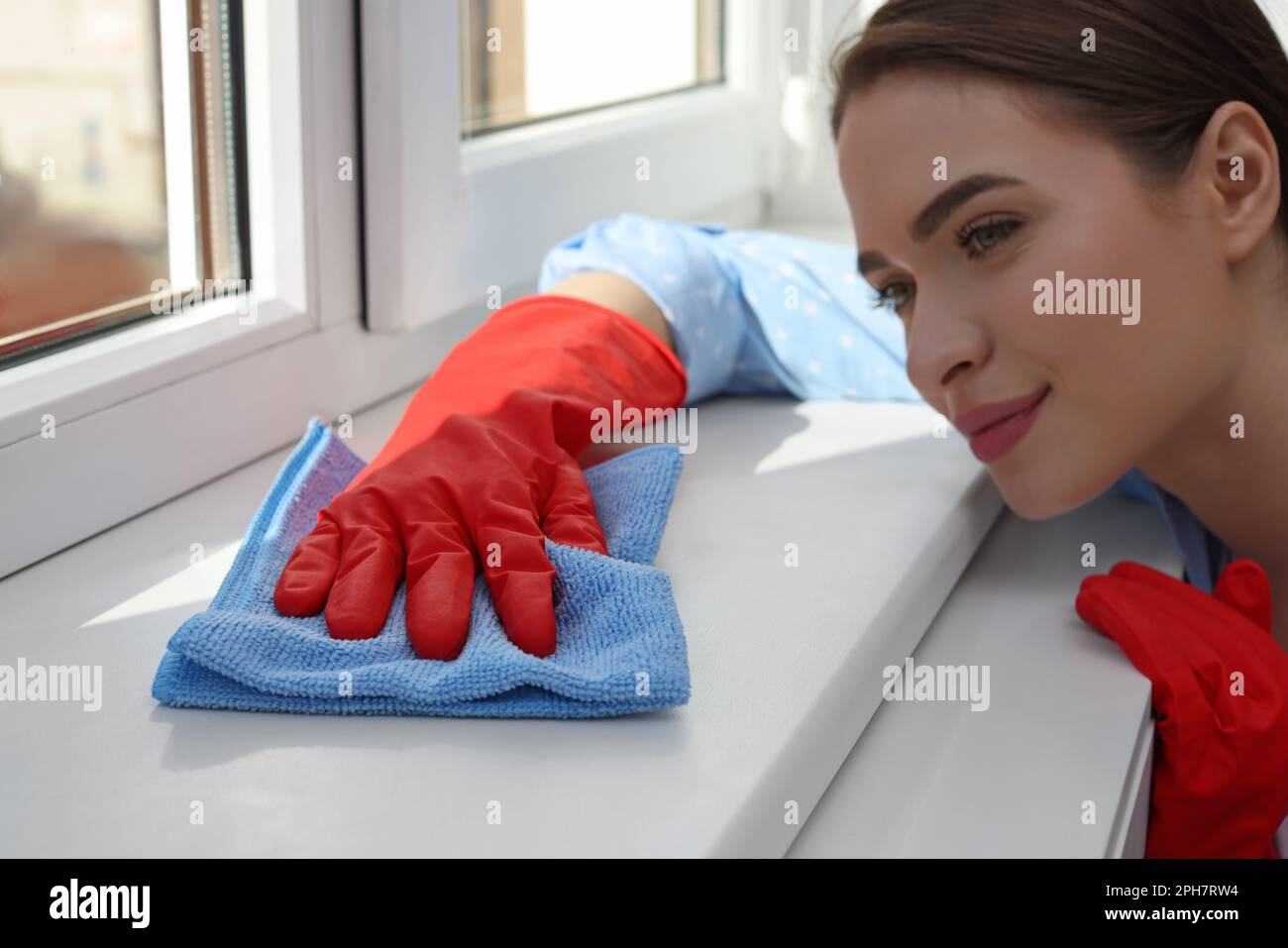 Une jeune femme nettoie le rebord de la fenêtre avec un chiffon à la maison Banque D'Images