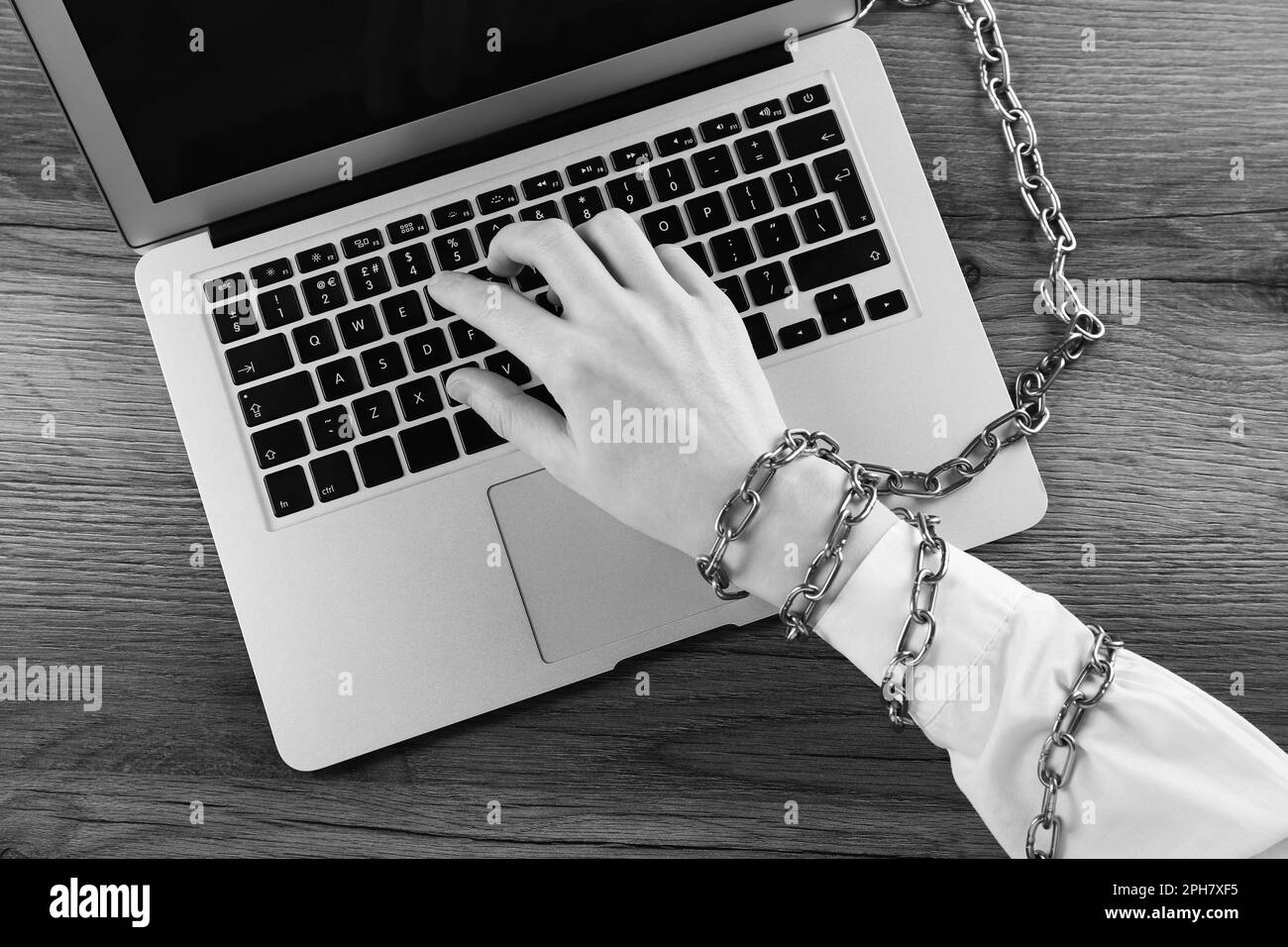 Vue de dessus d'une femme à main chaînée utilisant un ordinateur portable sur une table en bois, effet noir et blanc. Dépendance à l'Internet Banque D'Images