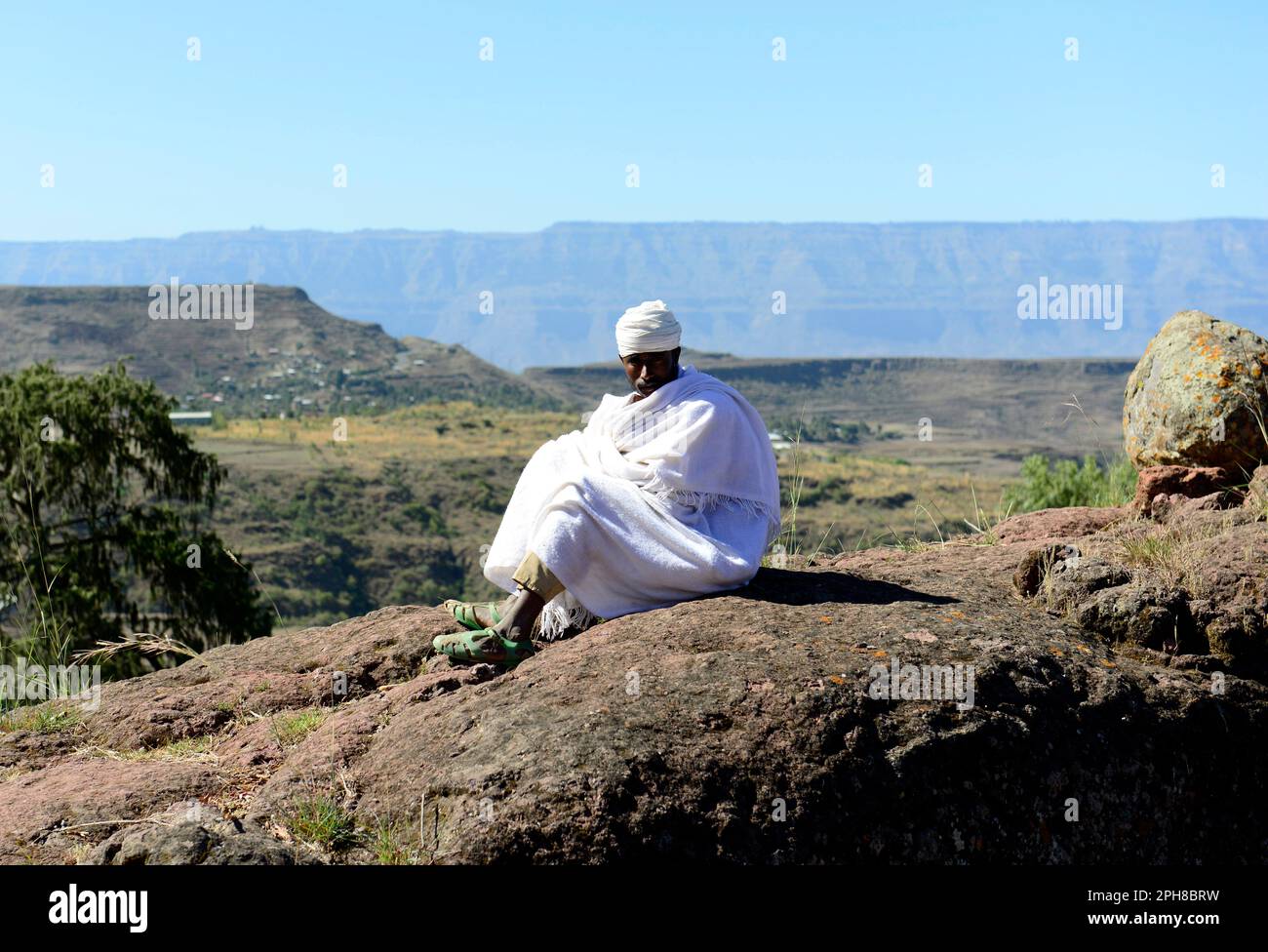 Un prêtre orthodoxe éthiopien assis au-dessus d'une église Rock-hewn à Lalibela, en Éthiopie. Banque D'Images