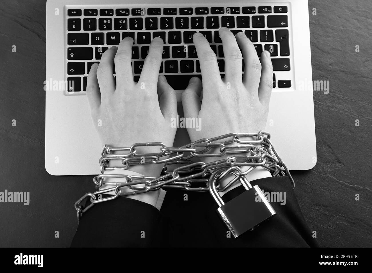 Vue de dessus d'une femme à mains chaînées utilisant un ordinateur portable sur une table sombre, effet noir et blanc. Dépendance à l'Internet Banque D'Images