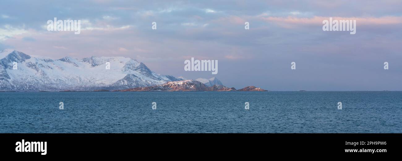 Morgenstimmung auf der Insel Senja und Kvaløya im Winter in Norwegen. DAS Morgenrot färbt schneebematte Berge und Wolken rötlich, lits Haus am Ufer Banque D'Images