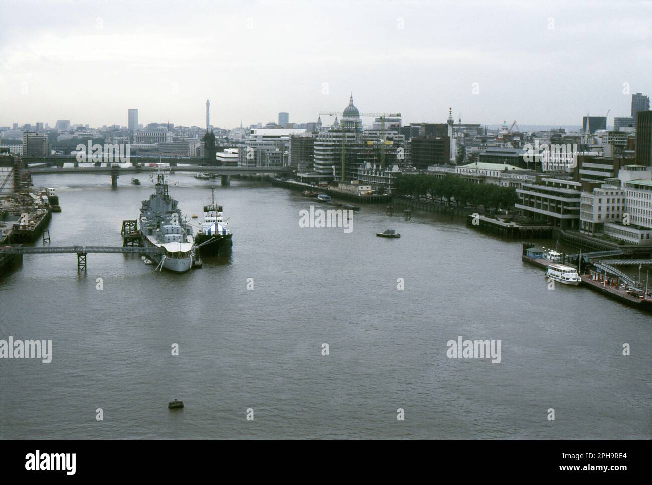 Londres. 1984. Vue vers l'ouest depuis le dernier étage du Tower Bridge, enjambant la Tamise à Londres, en Angleterre. Amarré sur la rivière est la deuxième période de la guerre mondiale Royal Navy Battlecruiser, H.M.S. Belfast, avec un autre navire à côté. Au-delà se trouve London Bridge et Cannon Street Railway Bridge. Sur la rive nord, le bâtiment Northern & Shell, situé au 10 Lower Thames Street, est en cours de construction. La tour de la poste, la cathédrale Saint-Paul et le monument sont visibles sur la ligne d’horizon. Banque D'Images