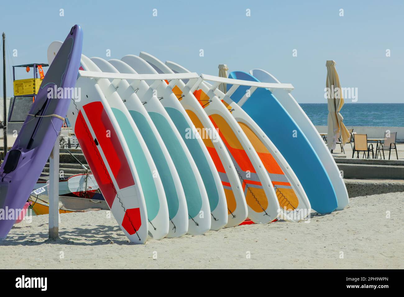 Support avec planches de paddle colorées et kayak sur le sable près de la mer Banque D'Images Support avec planches de paddle colorées et kayak sur le sable près de la mer Banque D'Images