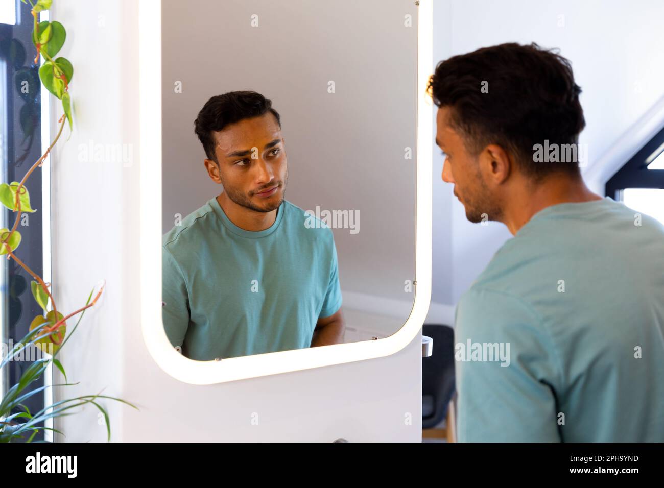 Homme biracial se regardant dans le miroir de salle de bains Banque D'Images
