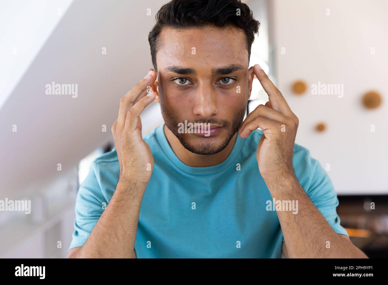 Homme biracial touchant son visage, regardant dans le miroir de salle de bains Banque D'Images