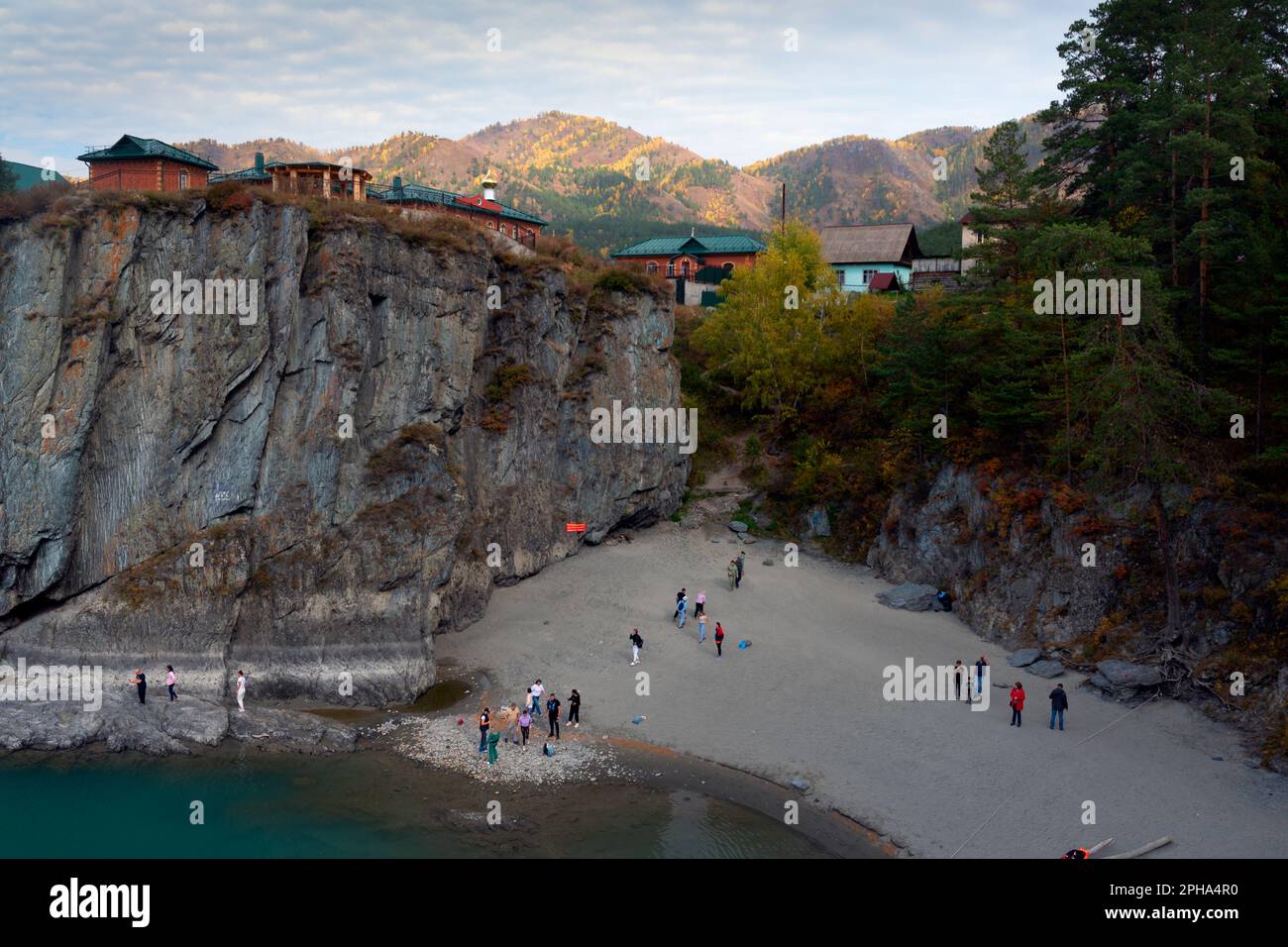 Les personnes qui se reposent marchent sur une plage de sable près d'une falaise en pierre avec une falaise avec des maisons de village au sommet de l'Altai en Sibérie. Banque D'Images