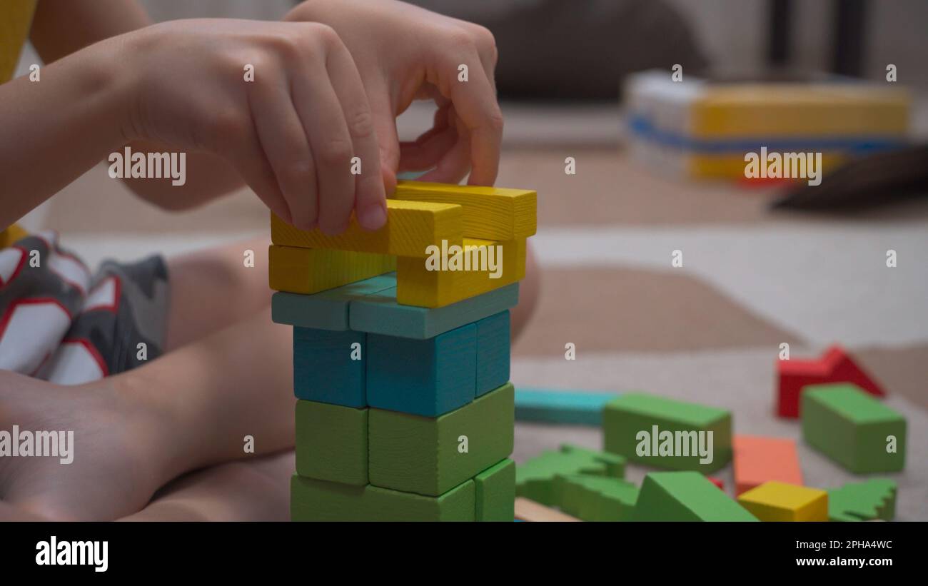 L'enfant construit une tour imaginaire de cubes de bois multicolores assis sur le sol dans sa chambre parmi un grand nombre de jouets. Le concept de la de Banque D'Images