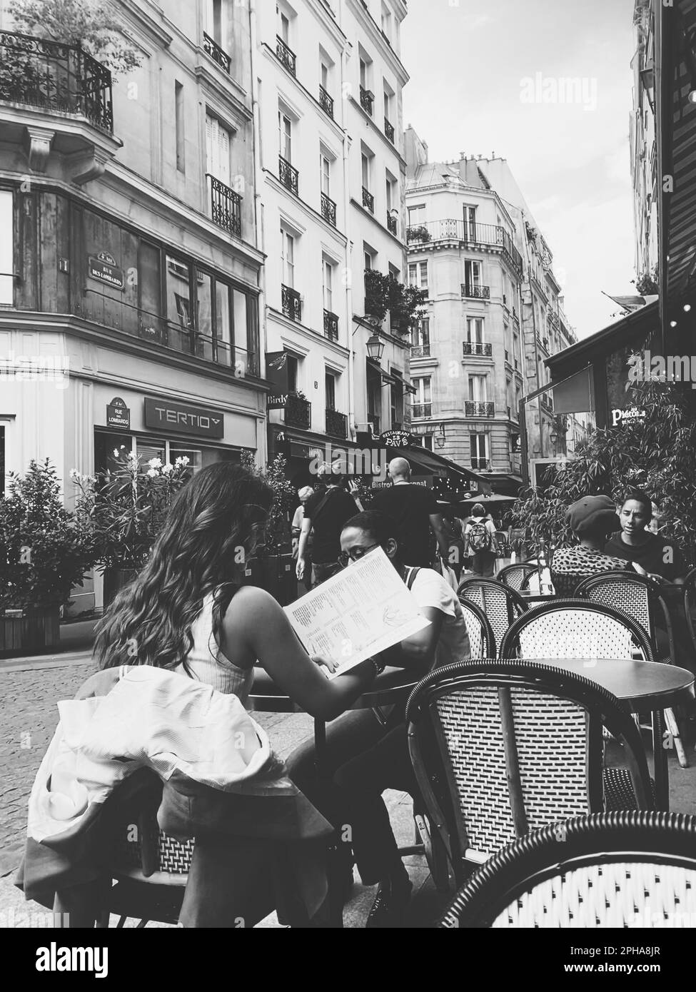 Une échelle de gris verticale d'une jeune femme attrayante appréciant la journée à l'extérieur dans un café Banque D'Images