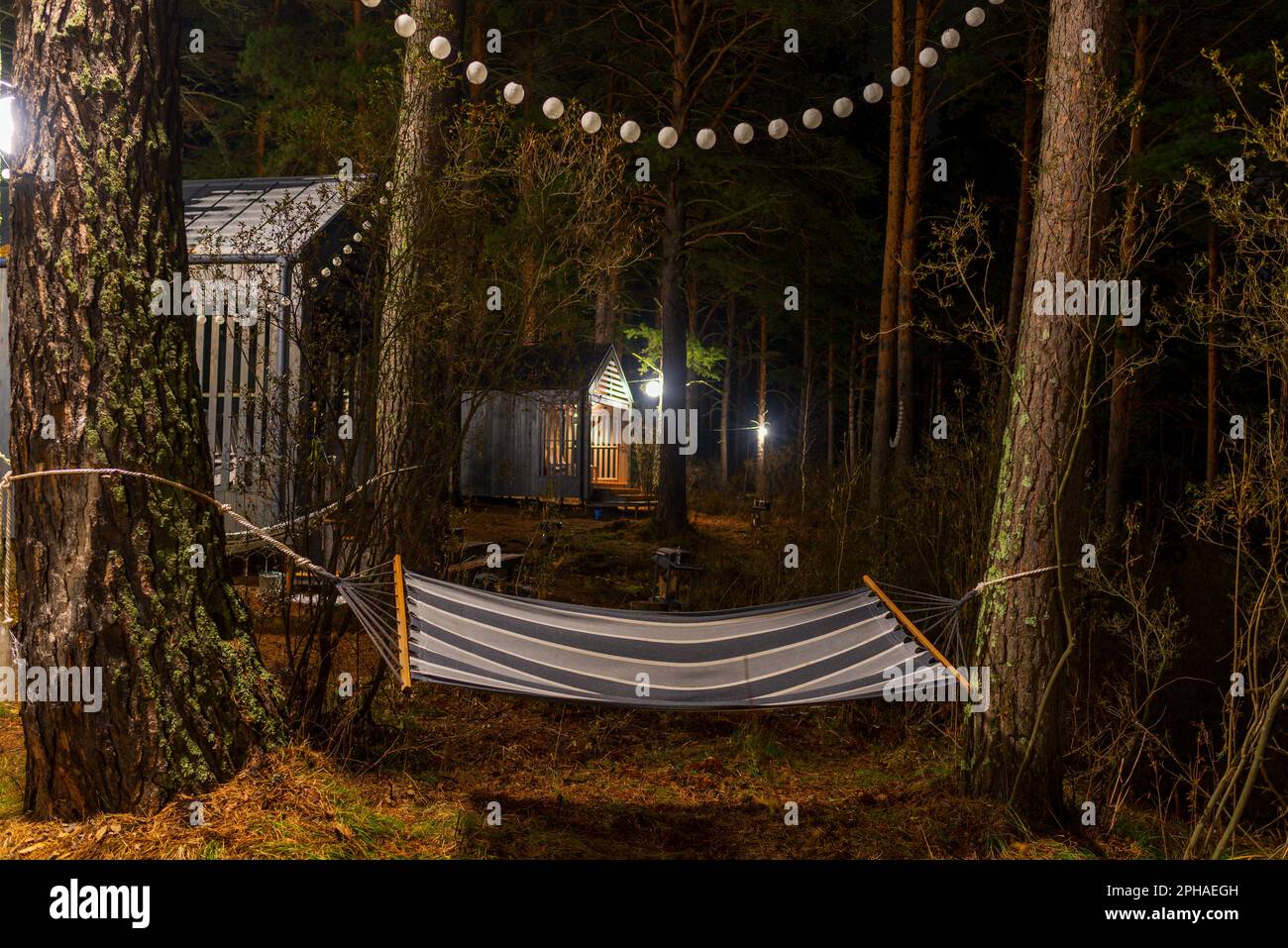 Un hamac rayé est suspendu entre les arbres sous les guirlandes la nuit,  près des maisons de vacances de l'Altaï Photo Stock - Alamy