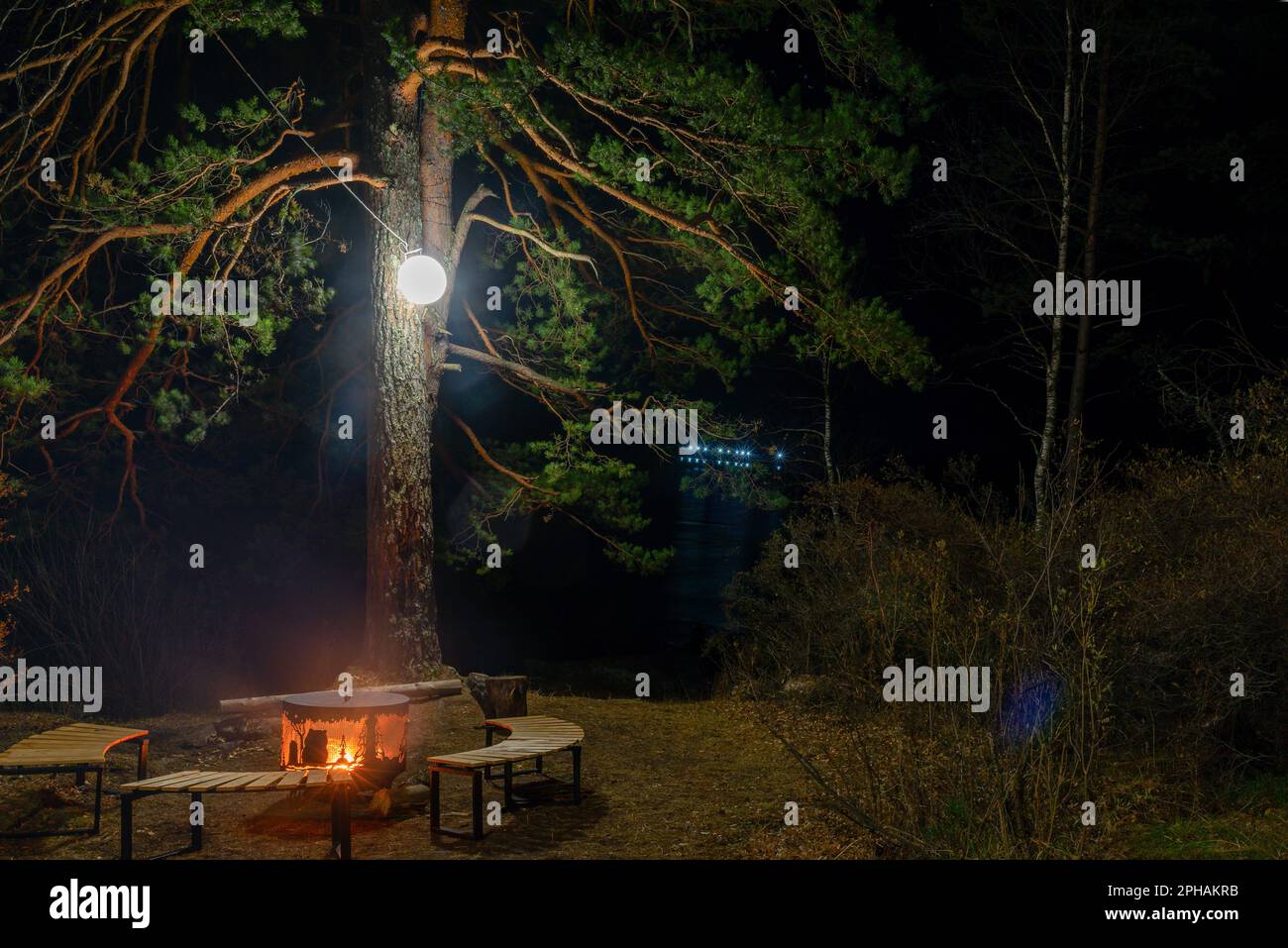 Un foyer, un foyer en métal entouré de bancs en bois se dresse la nuit sous un arbre avec une lanterne et un feu sur les rives de la rivière Katun. Banque D'Images