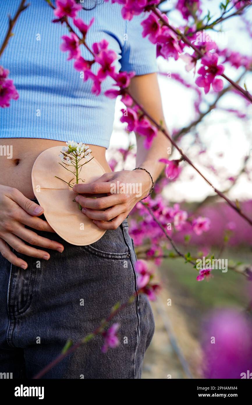 jeune femme méconnaissable dans un champ de fleurs roses avec un sac d'ostomie au printemps. jour du cancer du côlon Banque D'Images