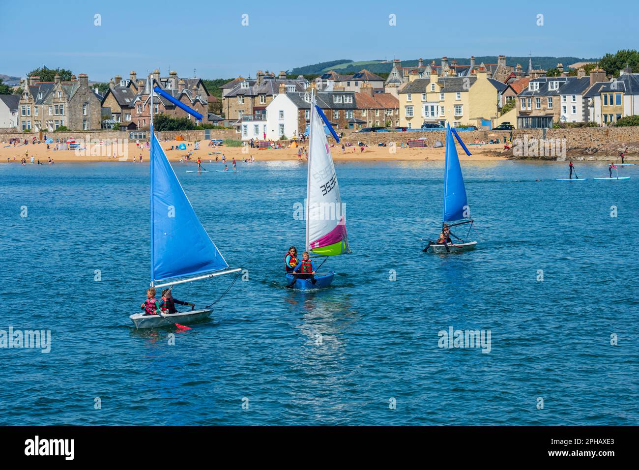 Les jeunes qui profitent du soleil d'été naviguent à bord d'un canot pneumatique dans le port d'Elie, avec la plage et la ville d'Elie en arrière-plan - Elie, Neuk est de Fife, Écosse, Royaume-Uni Banque D'Images