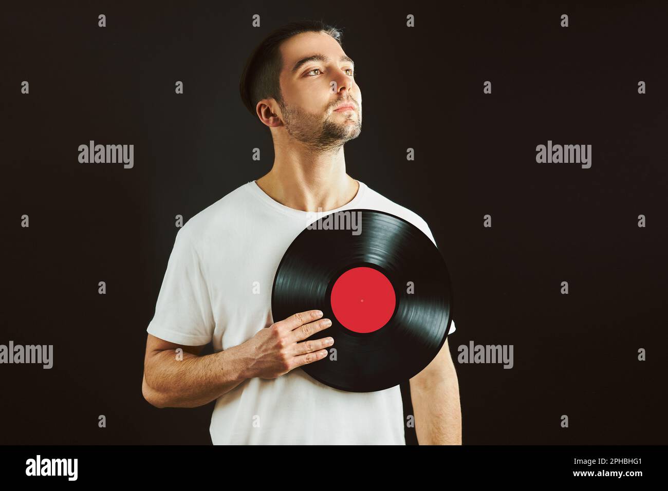 Homme tenant un disque en vinyle au-dessus du cœur. La passion de la musique. Style musical vintage. Homme tenant un ancien disque en vinyle debout sur fond noir. Musique rétro. Tribut Banque D'Images
