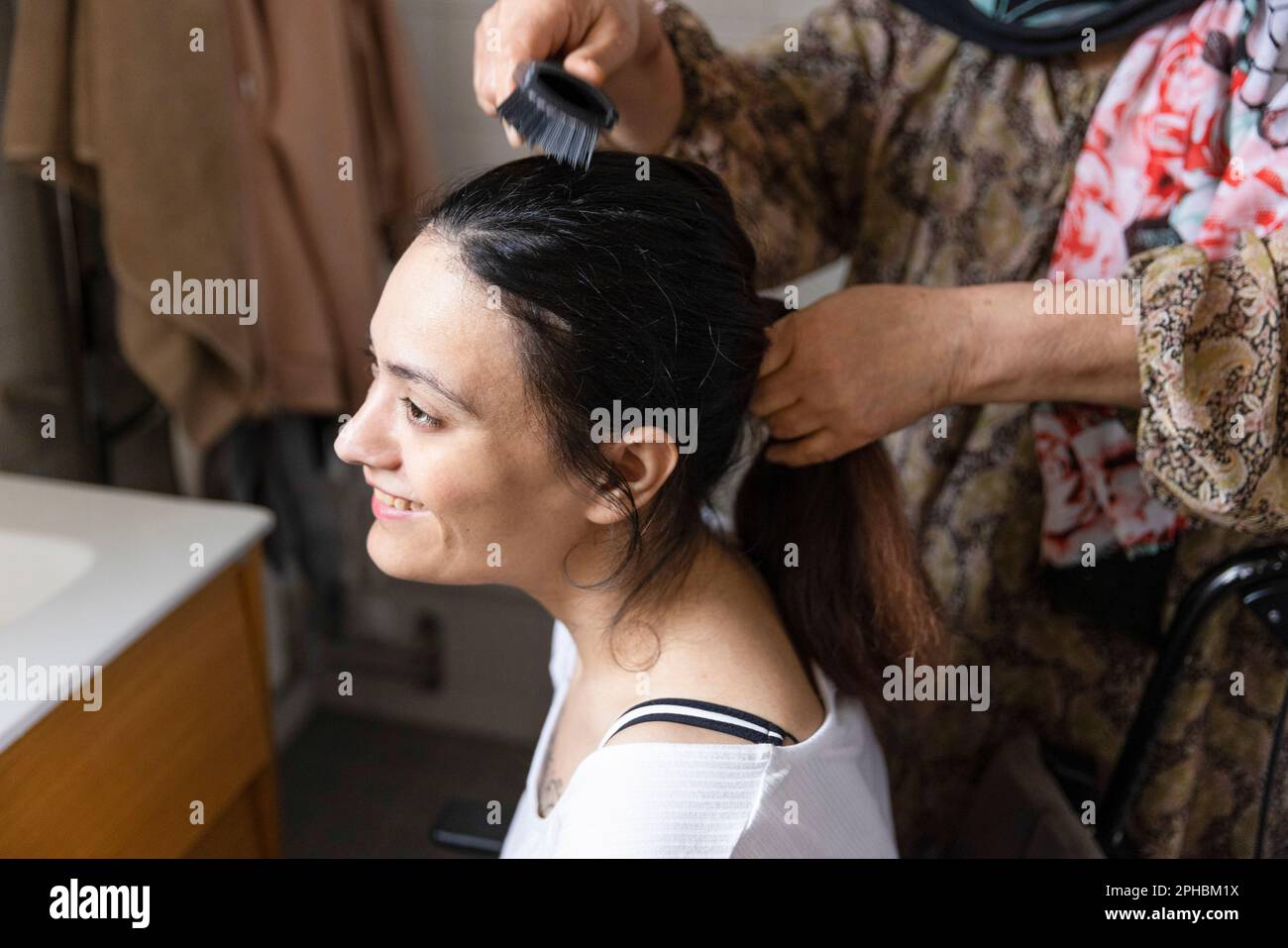 Mère peignant les cheveux de fille avec paraplégie dans la salle de bains à la maison Banque D'Images