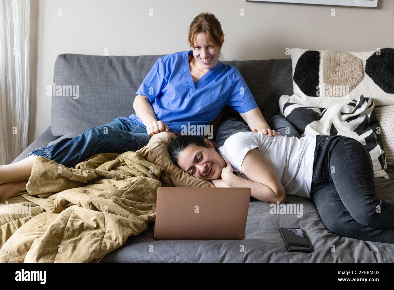 Une femme soignante et une femme handicapée regardant un film sur un ordinateur portable assis à la maison Banque D'Images