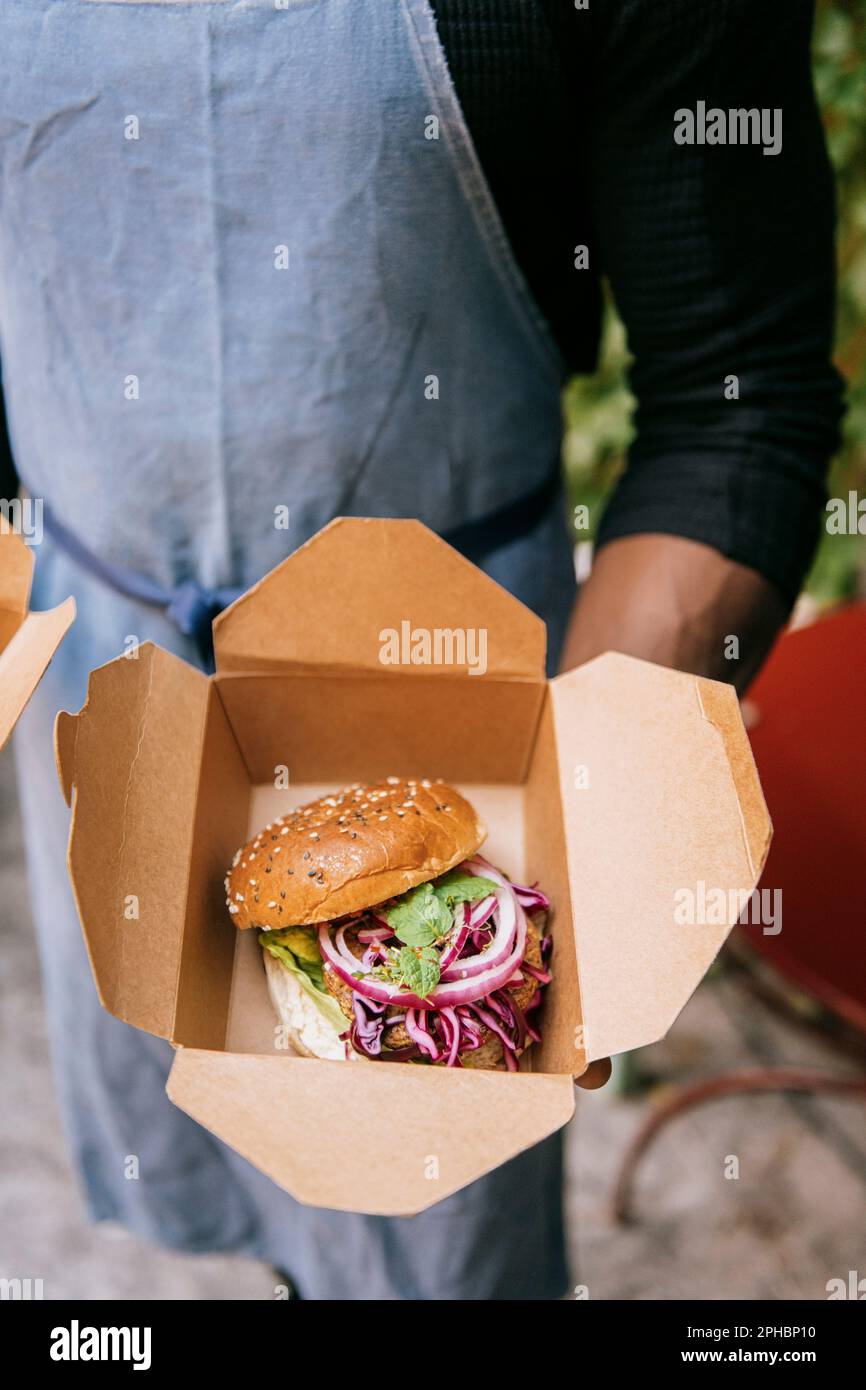 Vue en grand angle sur le propriétaire masculin du restaurant qui tient un hamburger fraîchement préparé dans une boîte Banque D'Images