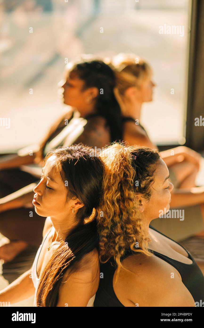 Les femmes amis s'asseyant dos à dos et s'exerçant pendant les cours de yoga Banque D'Images