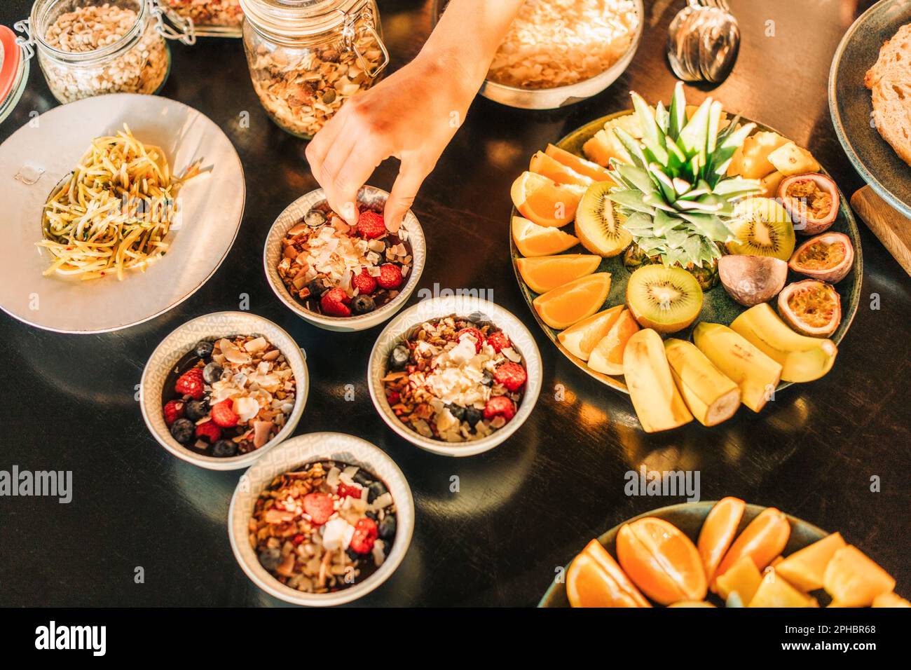 Main de la femme ramassant les baies du bol du petit déjeuner disposé sur une table Banque D'Images