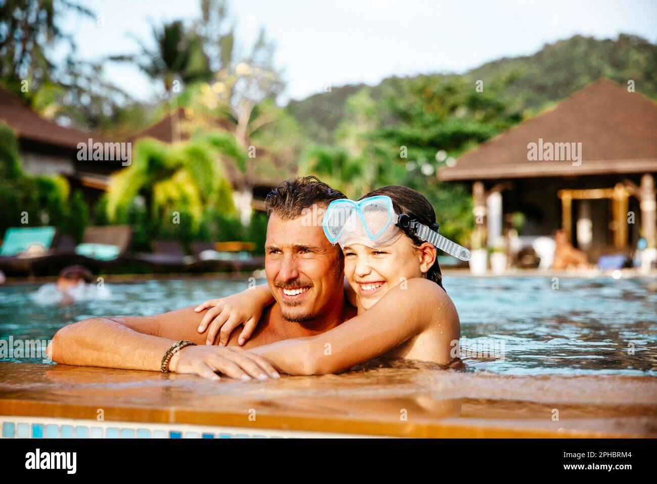 Fille souriante avec le bras autour du père dans la piscine à l'hôtel pendant les vacances Banque D'Images