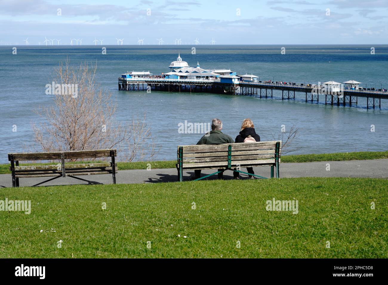 Llandudno Wales Royaume-Uni Mars 2023 deux adultes d'âge moyen se sont assis sur un banc de parc donnant sur la jetée de Llandudno Banque D'Images