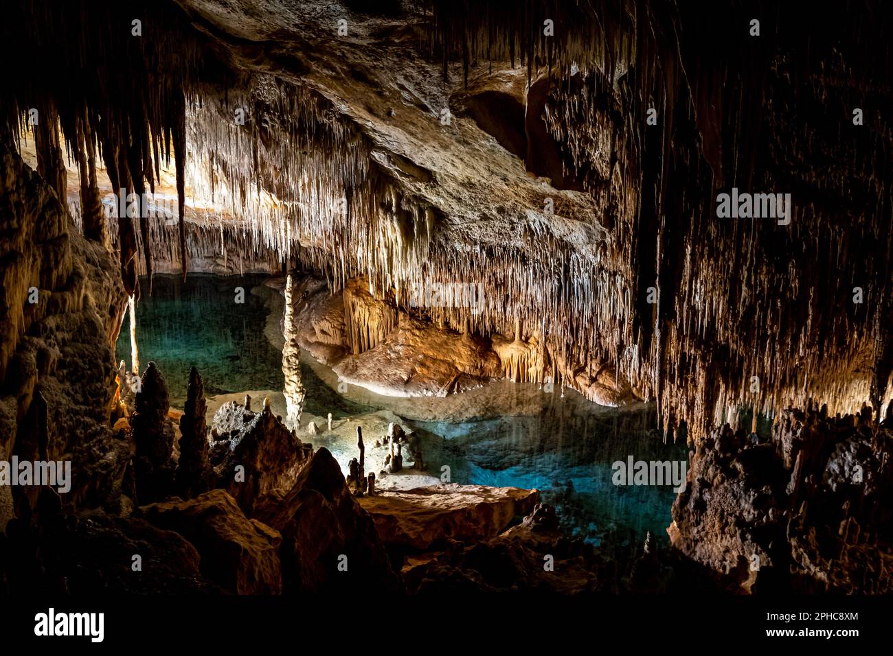 Lagon souterrain mystérieux avec eau bleue, stalagmites imposants et stalactites suspendues illuminés à l'intérieur de la majestueuse caverne sombre Cuevas del Drach Banque D'Images