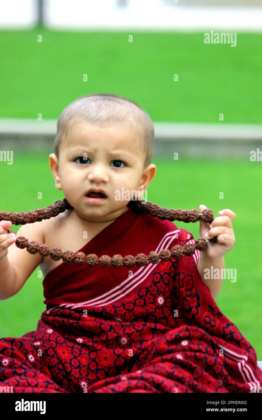 Un adorable petit garçon chauve est vêtu d'un avatar moine, portant un châle bordeaux, Rudraksh, et donnant une expression confuse. Banque D'Images