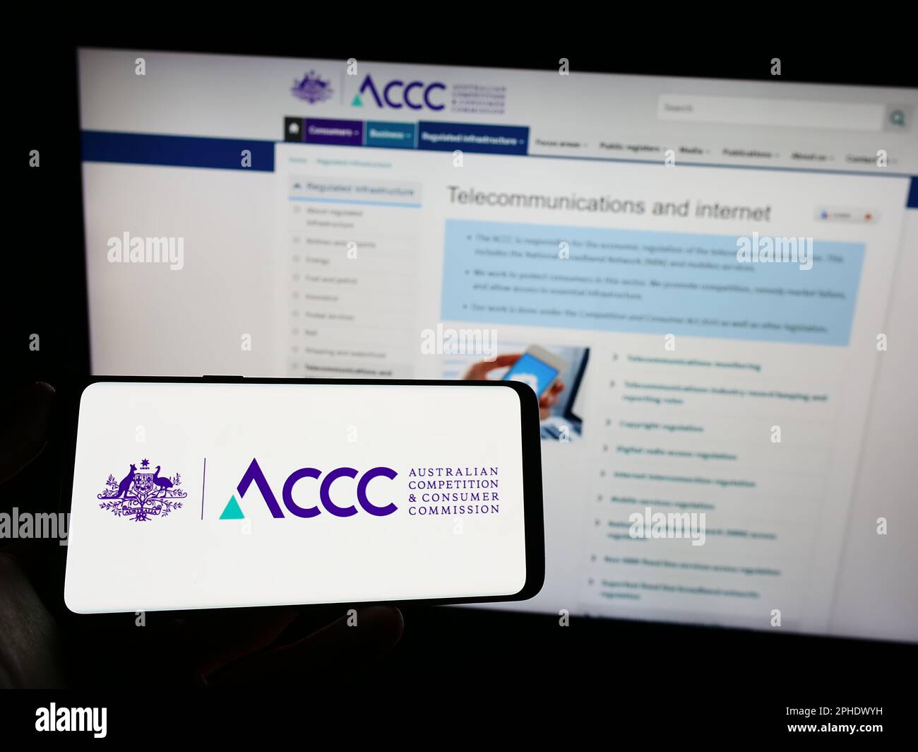 Personne tenant un téléphone portable avec le logo de la concurrence australienne et de la Commission des consommateurs sur l'écran en face de la page Web. Mise au point sur l'affichage du téléphone. Banque D'Images