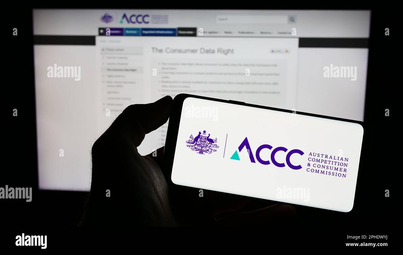 Personne tenant un téléphone portable avec le logo de la concurrence australienne et de la Commission des consommateurs à l'écran en face de la page Web. Mise au point sur l'affichage du téléphone. Banque D'Images