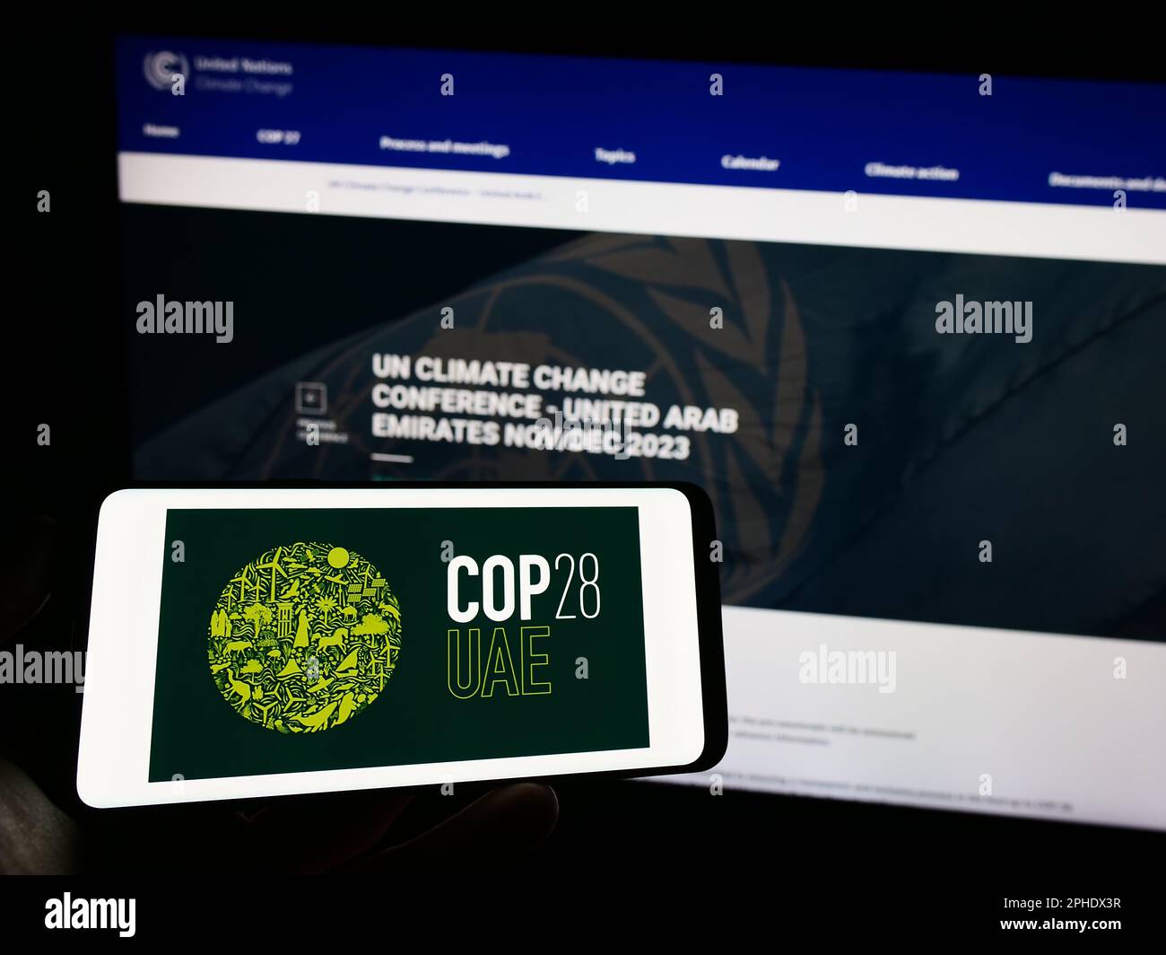 Personne tenant un téléphone portable avec le logo de la Conférence des Nations Unies sur le changement climatique COP28 (Dubaï) à l'écran en face de la page web. Mise au point sur l'affichage du téléphone. Banque D'Images