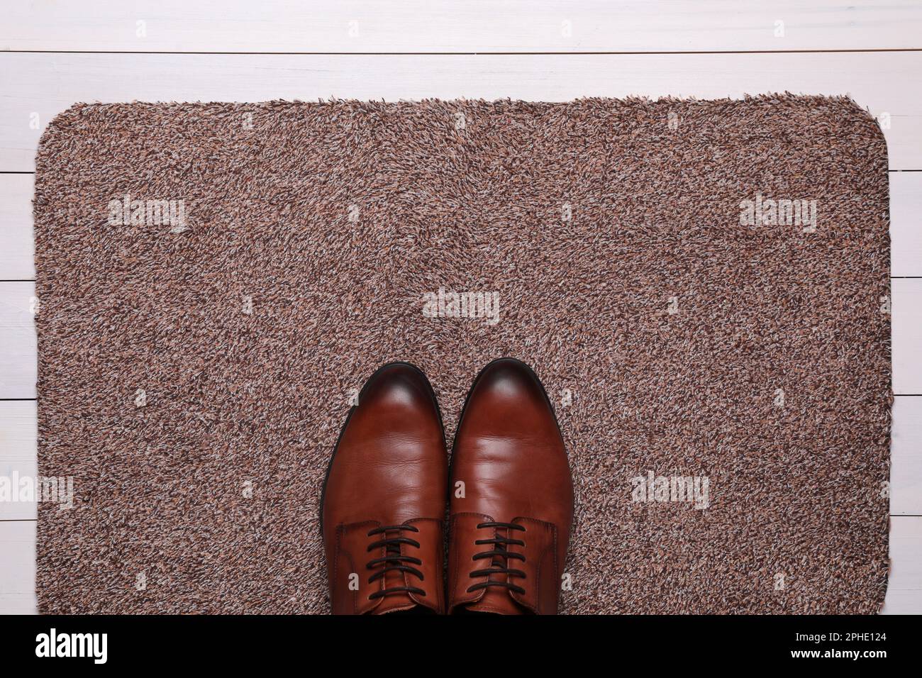 Nouveau tapis de porte propre avec des chaussures sur parquet blanc, vue de dessus Banque D'Images
