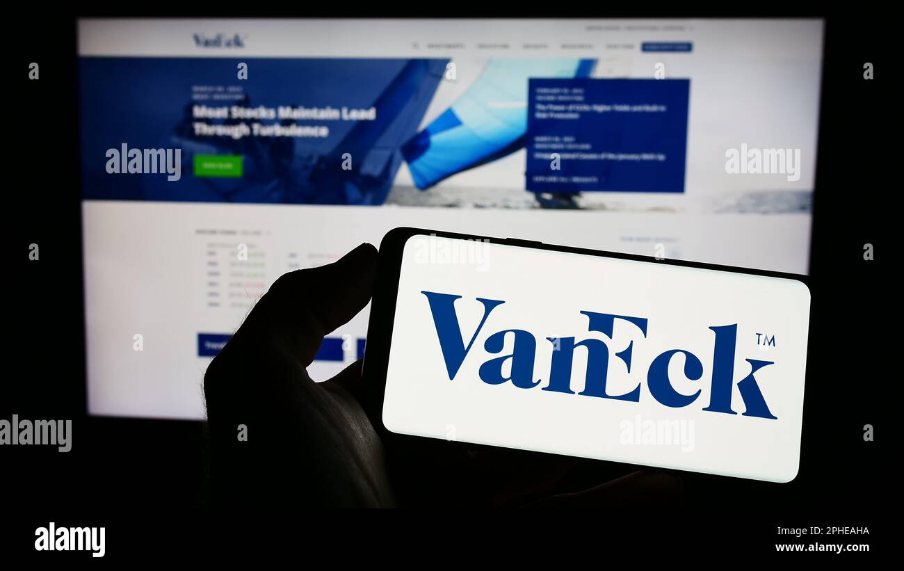 Personne tenant le téléphone portable avec le logo de la société américaine de gestion d'investissement VanEck sur l'écran en face de la page Web d'affaires. Mise au point sur l'affichage du téléphone. Banque D'Images