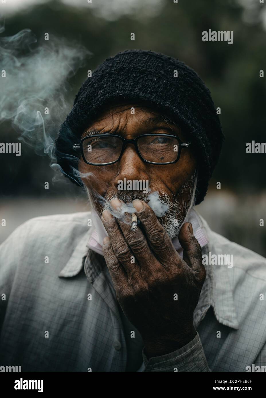 Un Indien âgé fume une cigarette allumée, exhalant la fumée de sa bouche Banque D'Images