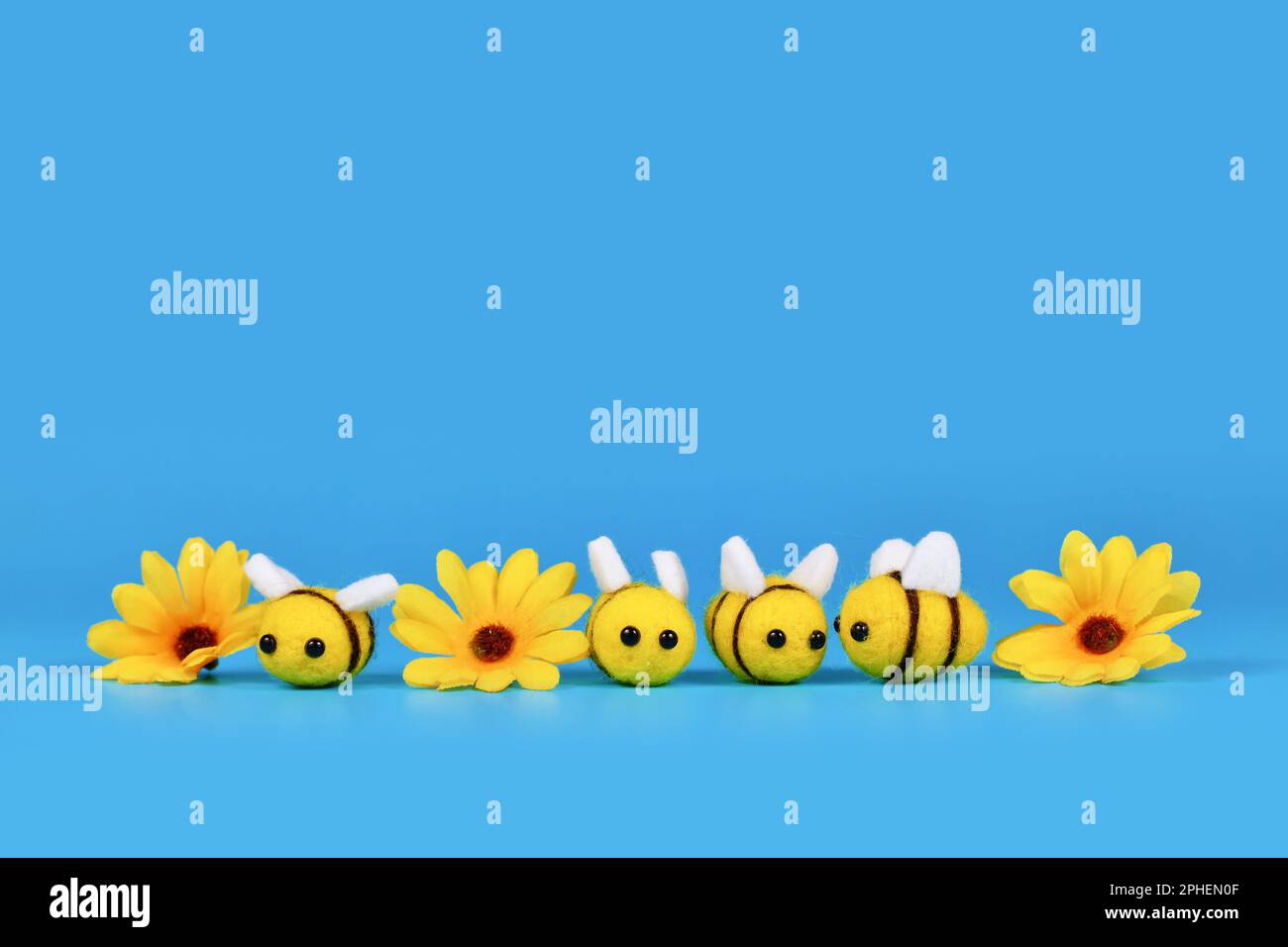 Des abeilles feutres mignons et des fleurs jaunes dans une rangée sur fond bleu avec espace de copie Banque D'Images
