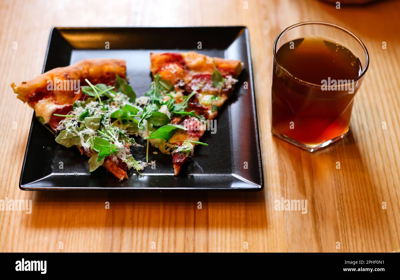 Deux pizzas au fromage et aux herbes sur une assiette noire et un verre de thé sur une table en bois Banque D'Images