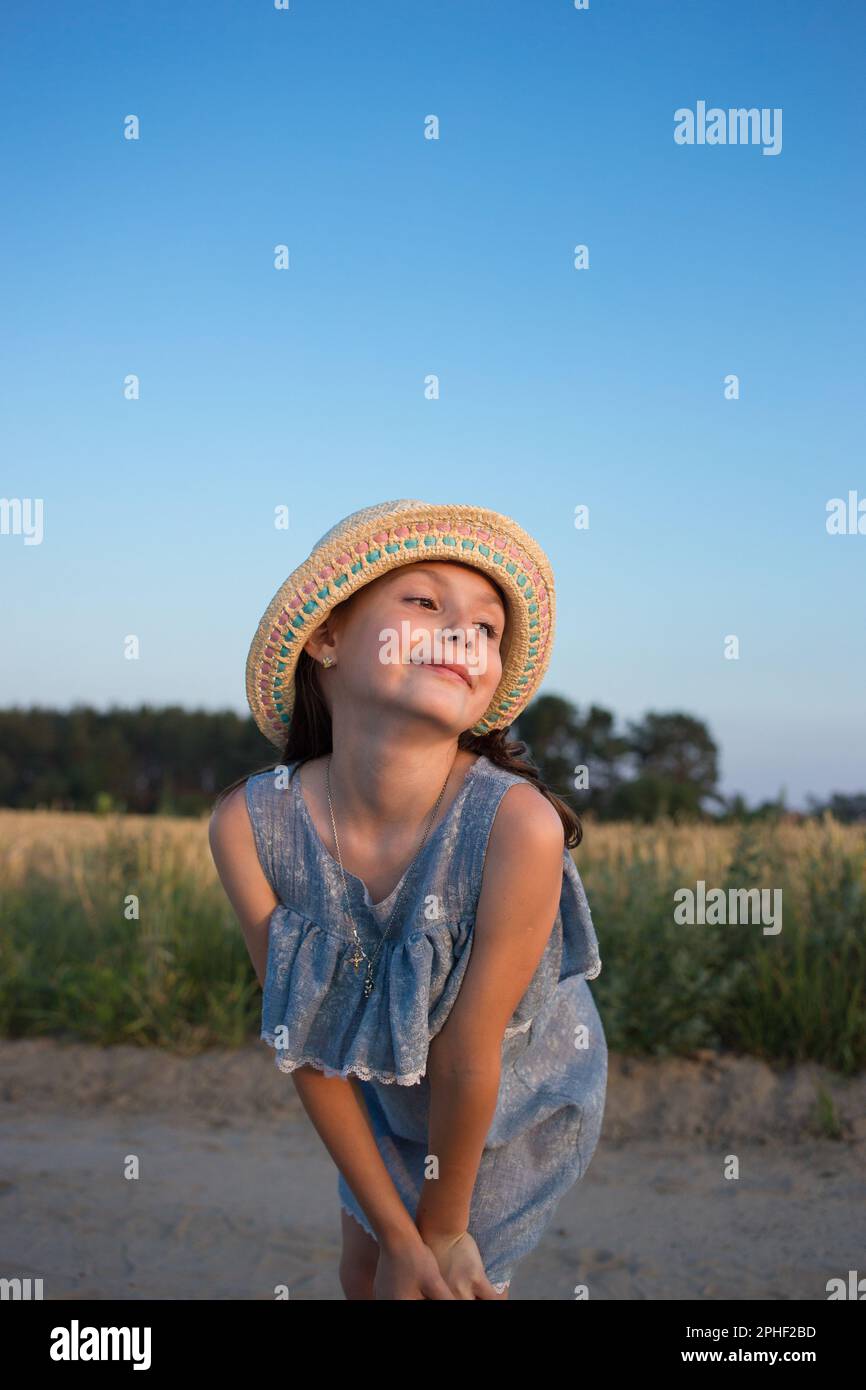 portrait d'une jolie fille de rêve de 7 ans dans une robe et un chapeau de paille dans la nature. bonne humeur, profitez de votre enfance. vacances, heure d'été. poser Banque D'Images