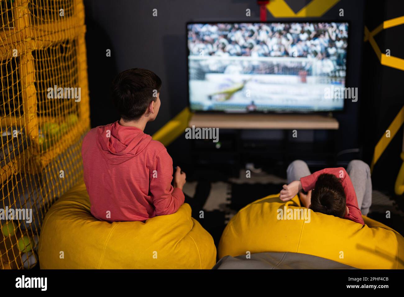 Deux frères jouant à la console de jeux vidéo de football, assis sur un pouf  jaune dans le centre de jeux pour enfants Photo Stock - Alamy