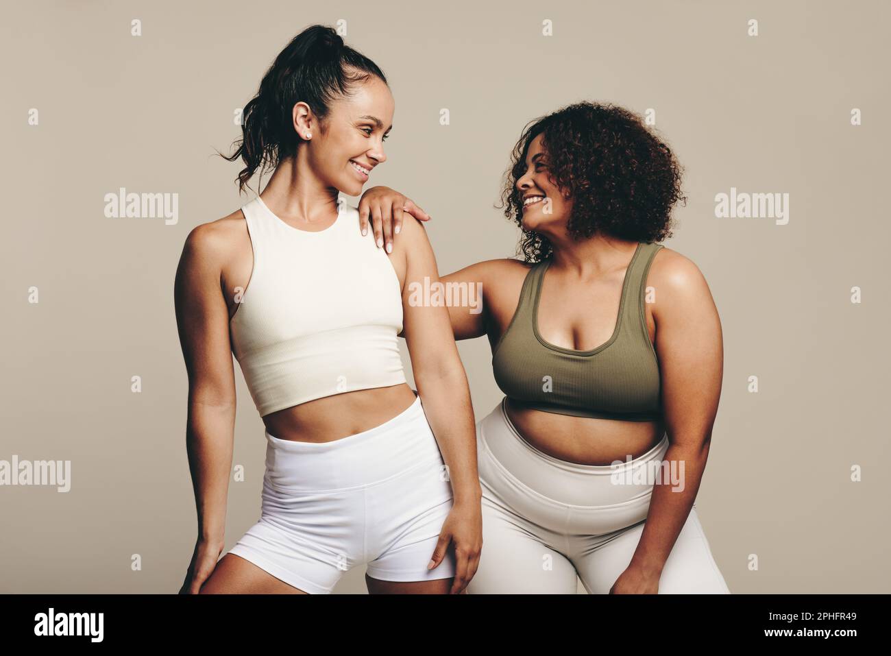 Les athlètes féminins de différentes formes de corps sourient lorsqu'ils se tiennent ensemble, vêtus d'un équipement d'entraînement. Deux jeunes femmes confiantes montrant leur dévouement à l'fi Banque D'Images
