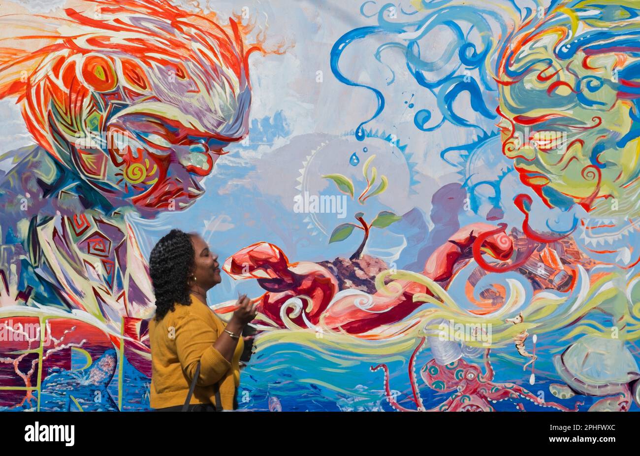 Cabrits, Dominique image de tête et d'épaule d'une femme locale portant un haut jaune marchant devant une toile de fond graffiti représentant un message environnemental. Banque D'Images