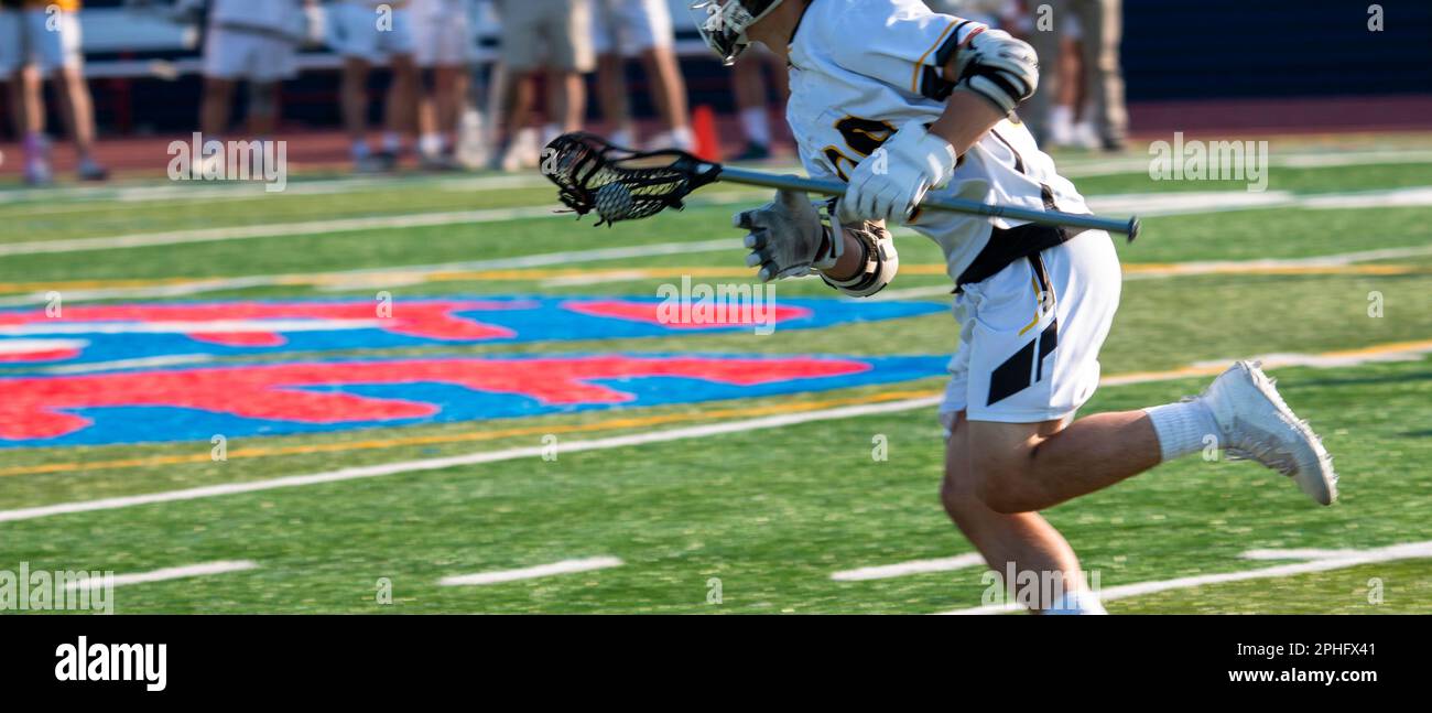 Joueur de crosse de lycée courant sur le terrain avec le ballon pendant un match. Banque D'Images