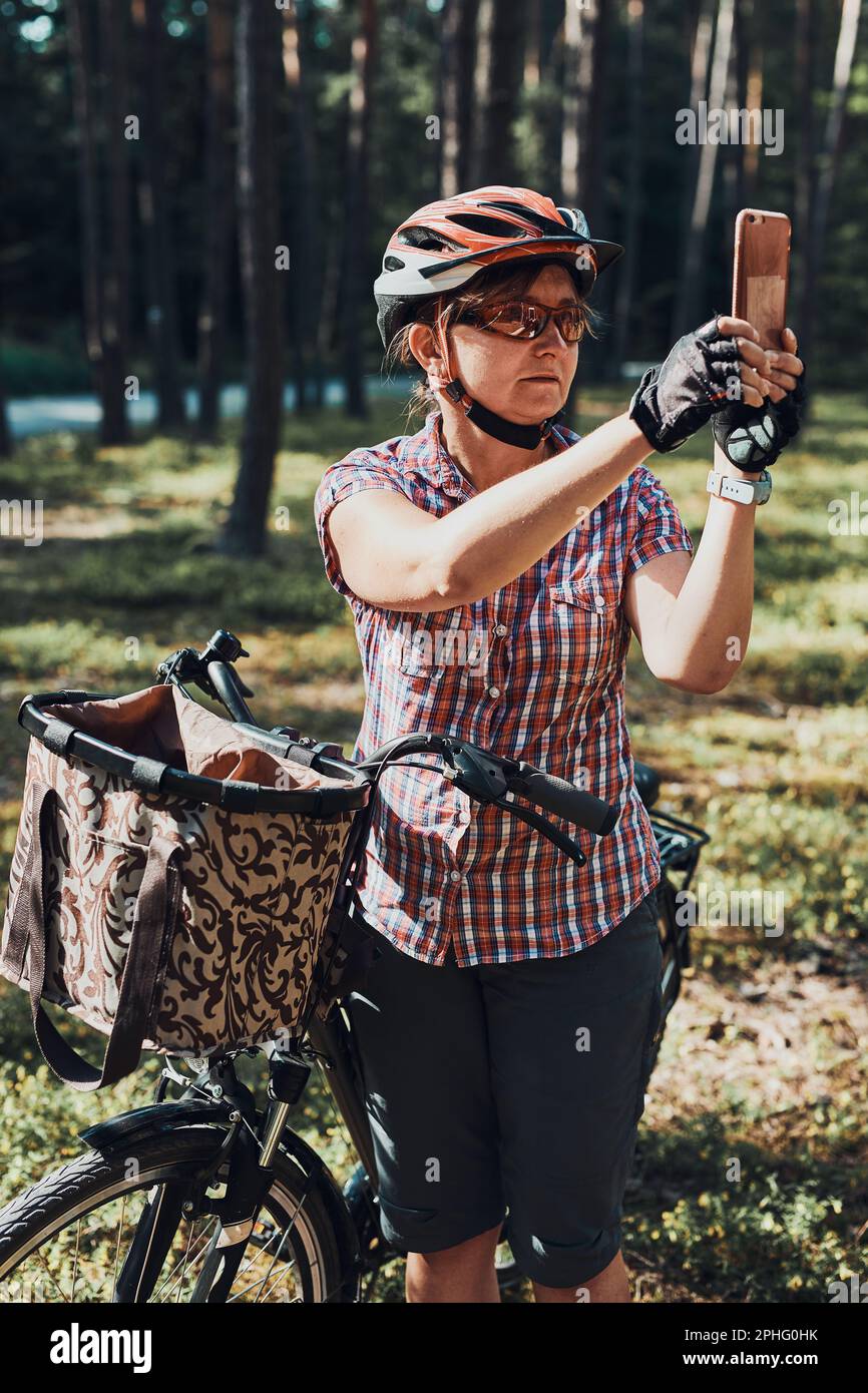 Femme active qui passe des vacances d'été gratuites dans une forêt lors d'un voyage à vélo en prenant des photos à l'aide d'un smartphone. Femme portant un casque de vélo et des gants Banque D'Images