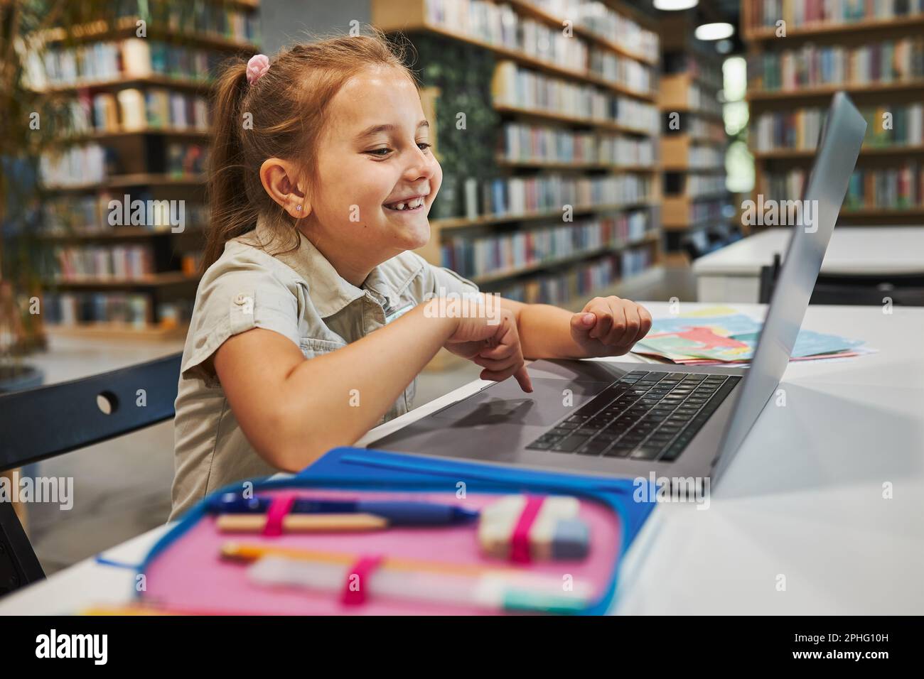 Étudiante gaie faisant ses devoirs à l'aide d'un ordinateur portable dans un club après l'école primaire. Retour à l'école. Enfant utilisant la technologie sur l'ordinateur élémentaire Banque D'Images
