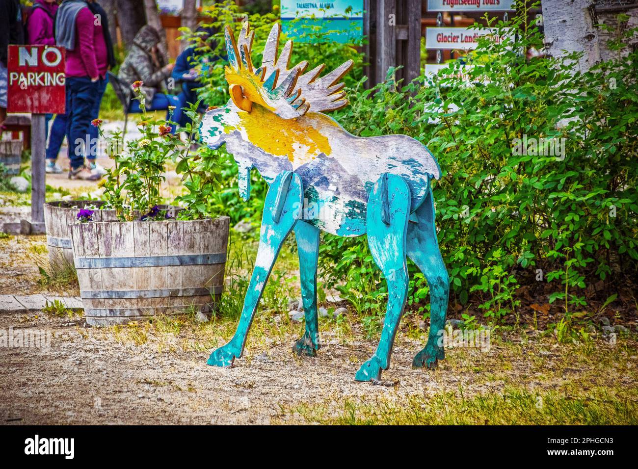 Le tourisme en Alaska - orignal en bois peint debout par des panneaux touristiques pour les entreprises et les jardinières de fleurs en bois - des gens méconnaissables alignés en b Banque D'Images