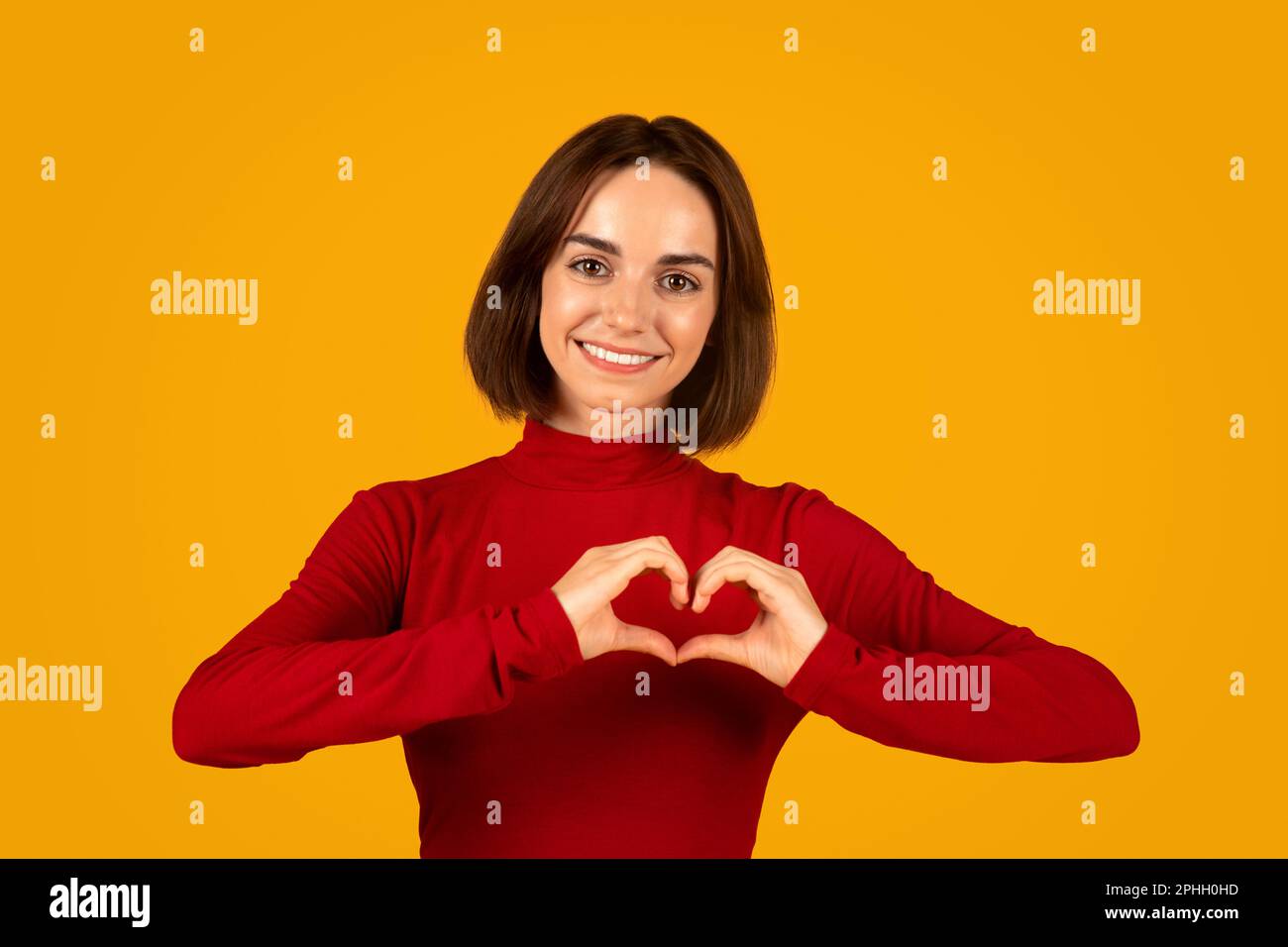 Jeune femme gaie tenant les mains sur la poitrine en forme de coeur Banque D'Images