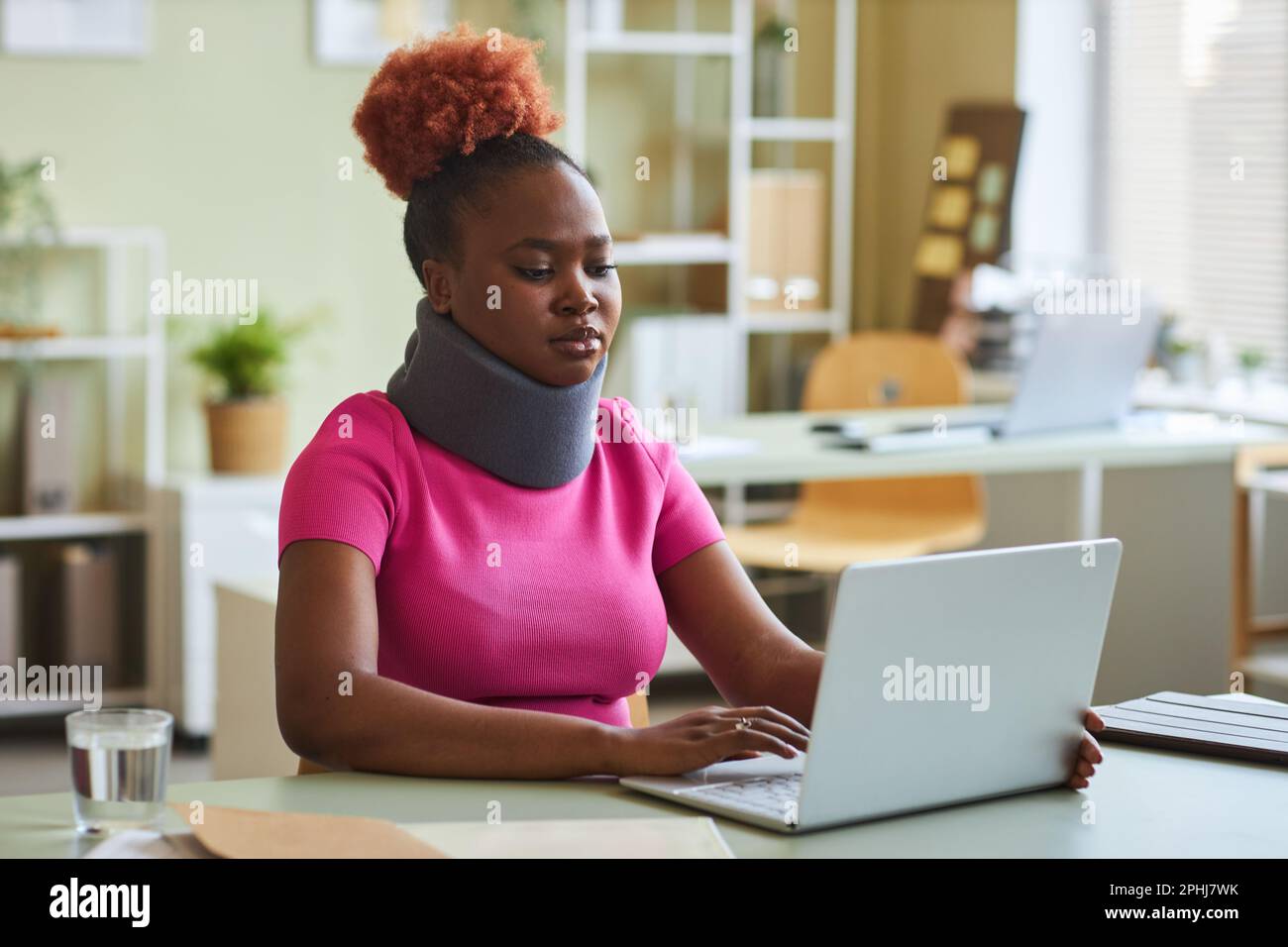 Portrait d'une jeune femme noire avec un corset de cou travaillant au bureau et utilisant un ordinateur portable Banque D'Images