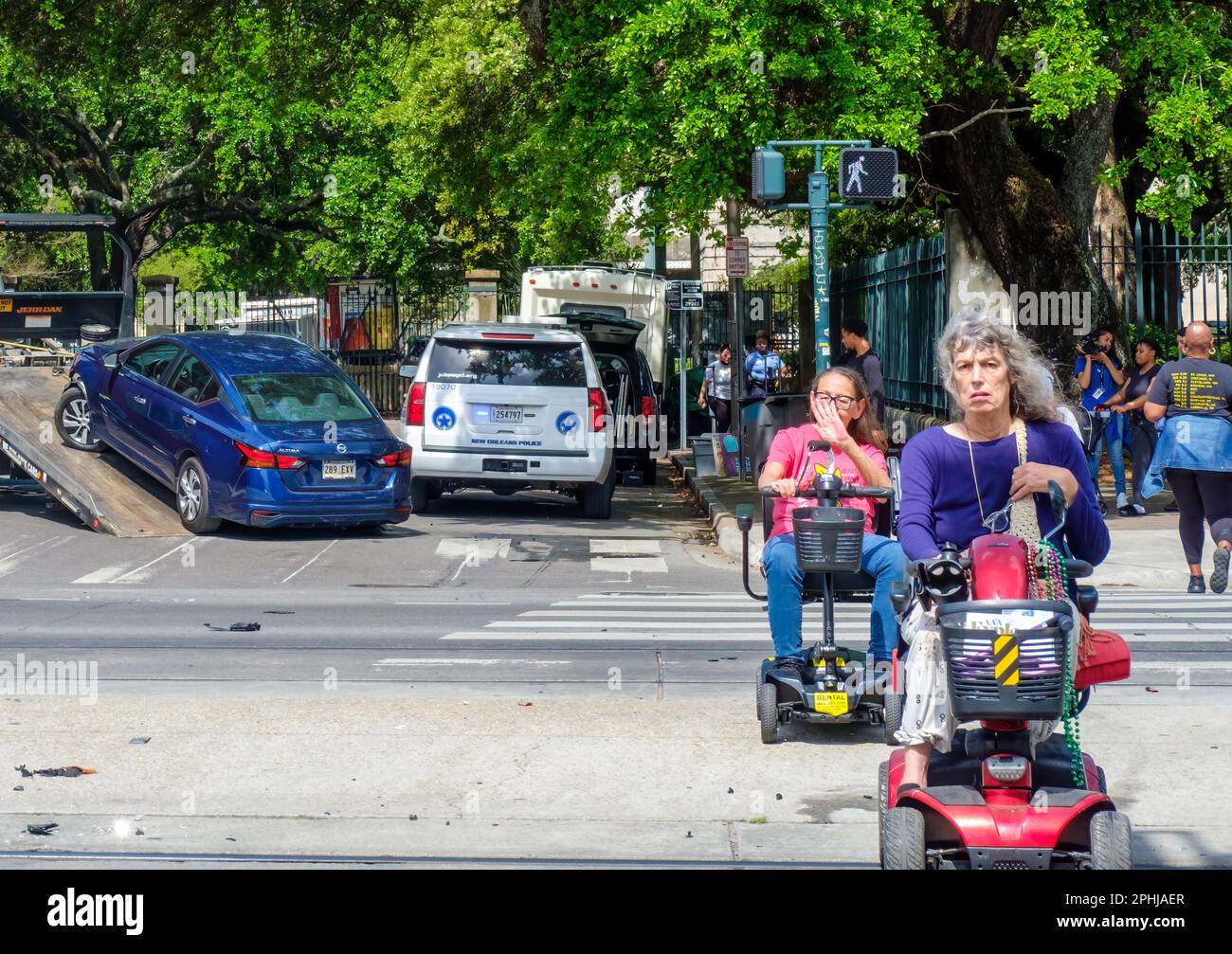 NEW ORLEANS, LA, États-Unis - 26 MARS 2023 : paysage urbain avec deux femmes handicapées sur leurs scooters motorisés dans un passage en croix et une voiture remorquée Banque D'Images