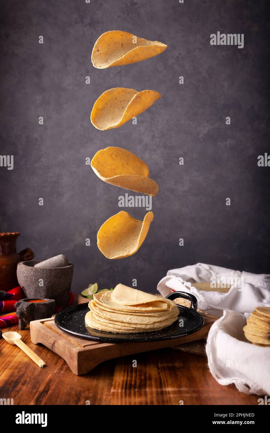 Tortillas de maïs tombant sur une plaque chauffante mexicaine dans un cadre typiquement mexicain avec une table rustique en bois et des molajetes en pierre. Banque D'Images